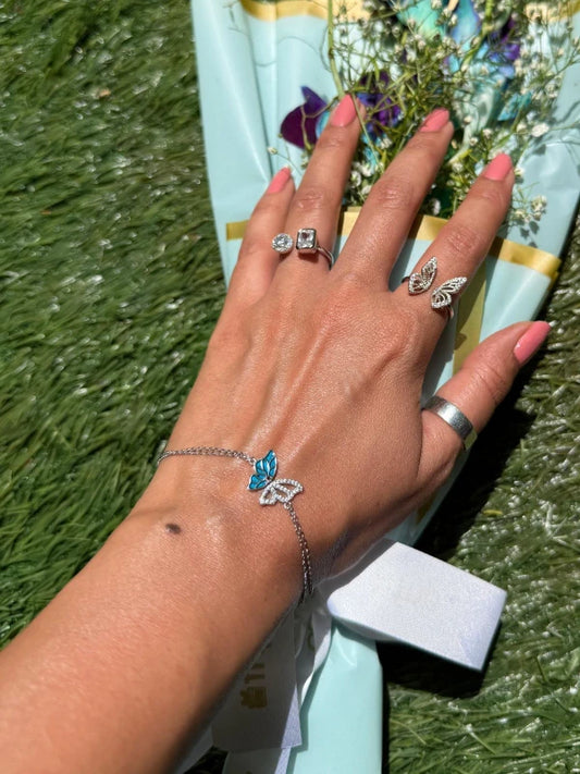 Hand wearing butterfly-themed jewelry with a scenic background