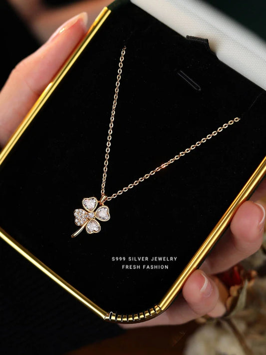 Four-leaf clover silver necklace held by a hand on a black card with gold border