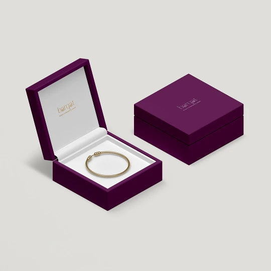 Gold bracelet in an open purple jewelry box on a light gray background