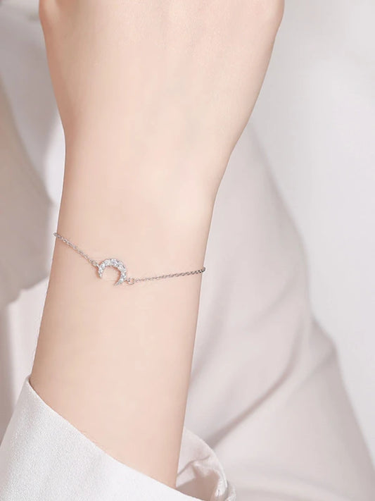 Silver bracelet with a rainbow charm on a wrist against a light background