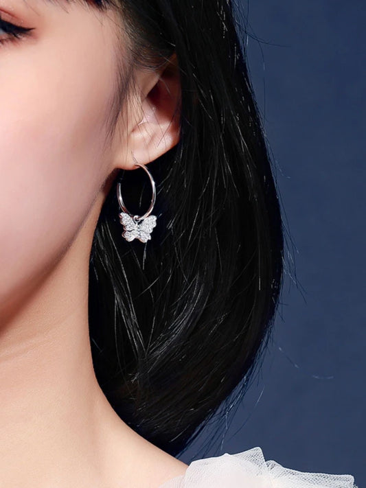 Close-up of a woman wearing a silver hoop earring with a butterfly pendant against a dark blue background.