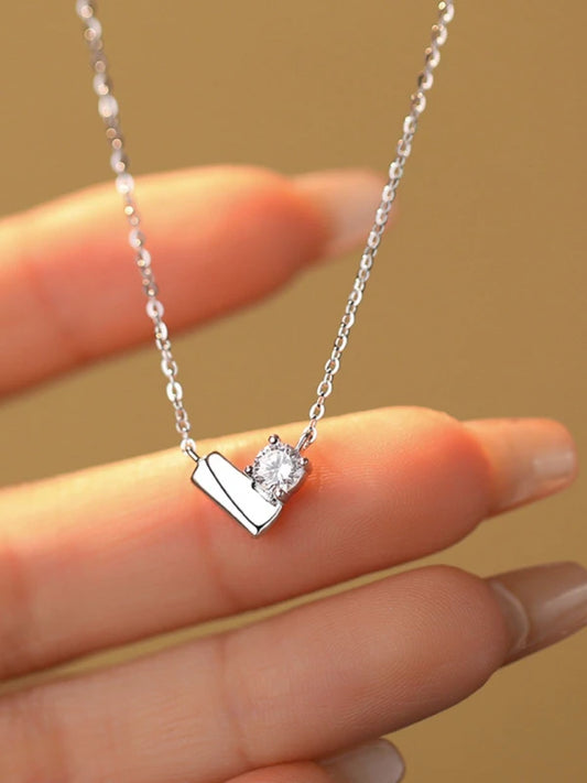 Silver necklace with a heart and diamond pendant held by a hand against a beige background