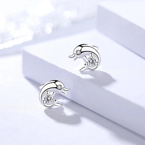 Silver dolphin-shaped earrings with clear gemstones on a white surface