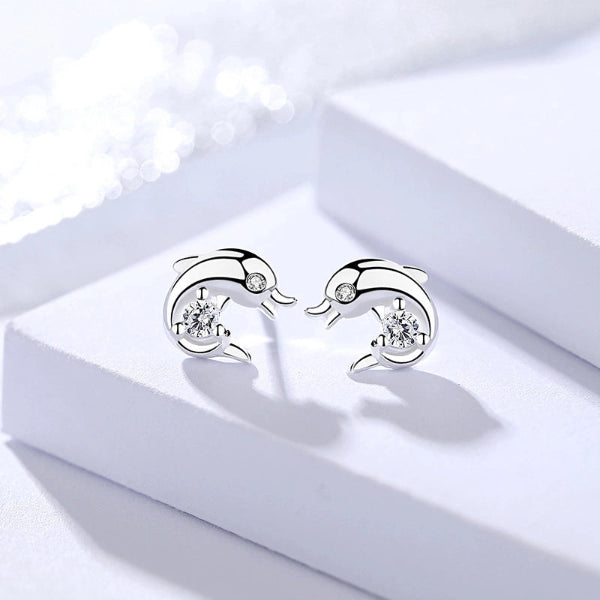 Silver dolphin-shaped earrings with clear gemstones on a white box