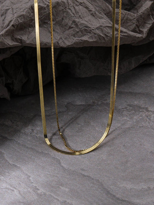 Double layered snake chain necklace on a dark textured surface