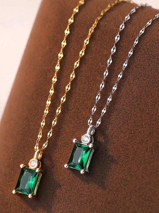 Two emerald green gemstone pendants on gold and silver chains against a brown background
