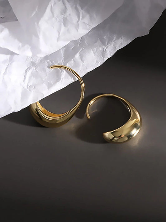 Gold hoop earrings on a dark surface with white paper