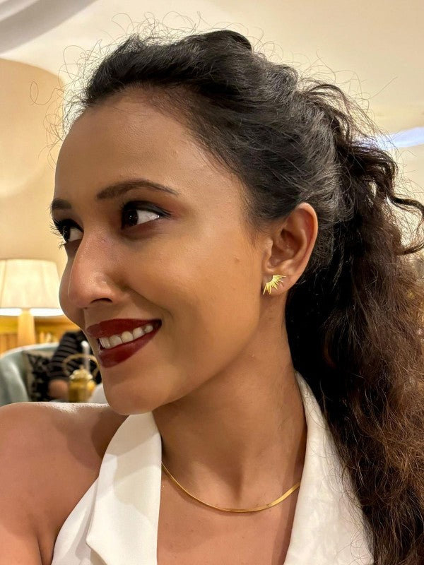 Woman with a ponytail wearing a gold earring and necklace, indoors.