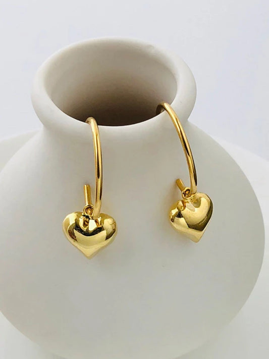 Gold heart-shaped earrings on a white ceramic vase