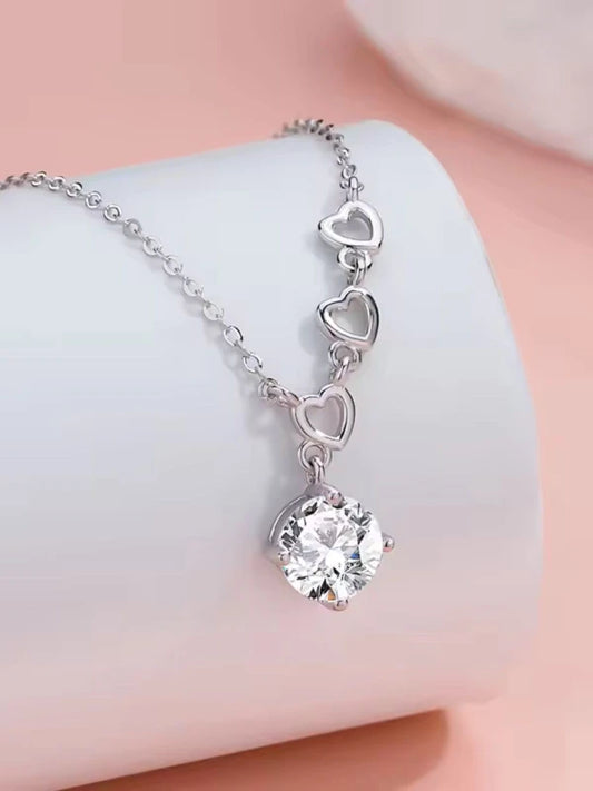 Silver necklace with heart-shaped links and a clear crystal pendant on a soft pink background