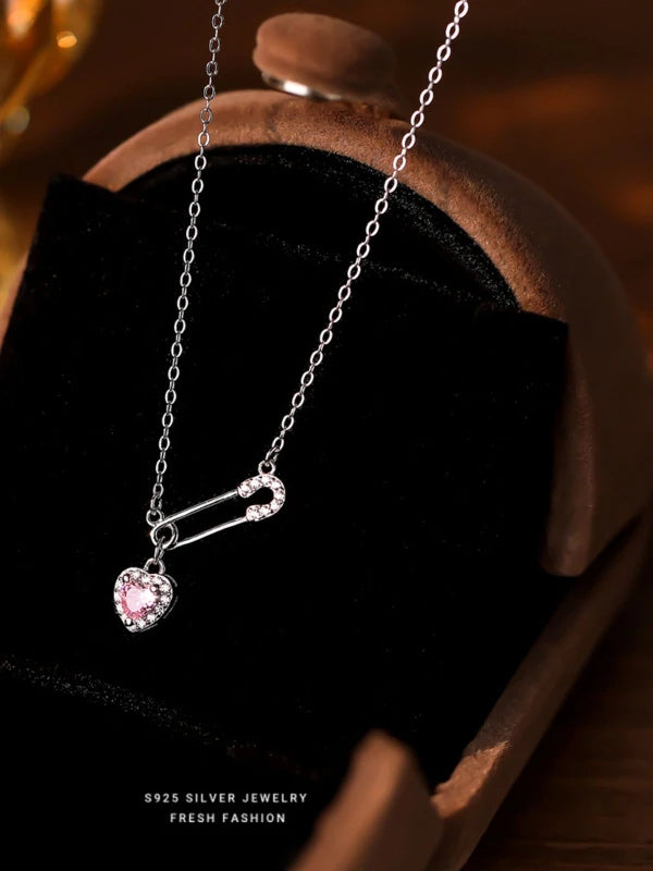 Silver necklace with a pink heart pendant on a dark surface