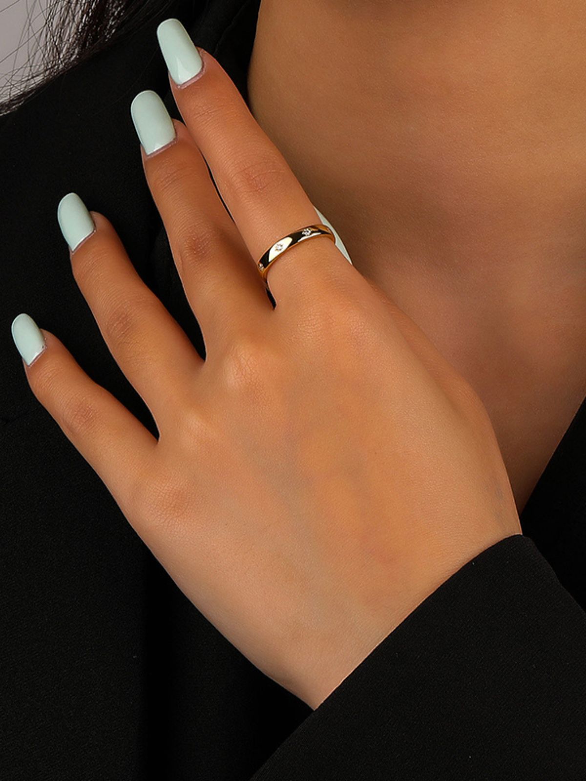 Hand with light green nail polish wearing a gold ring on a black background