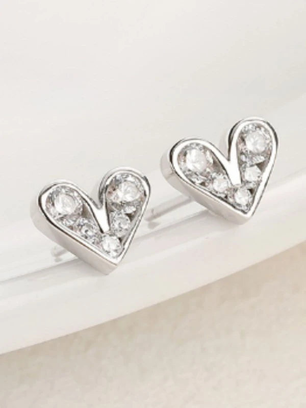 Heart-shaped silver earrings with clear gemstones on a light background