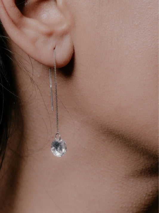 Close-up of an ear wearing a delicate silver earring with a clear gemstone.