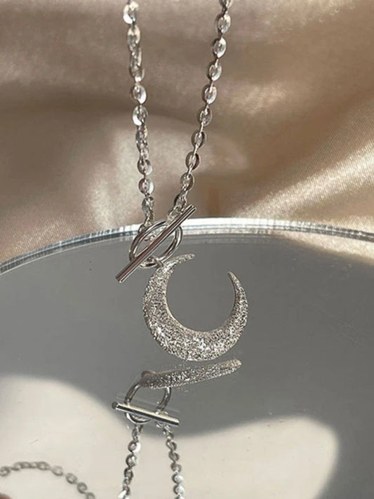 Silver necklace with a crescent moon pendant on a reflective surface.