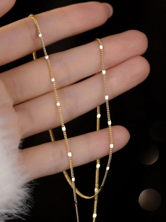 Gold chain necklace on a hand against a dark background