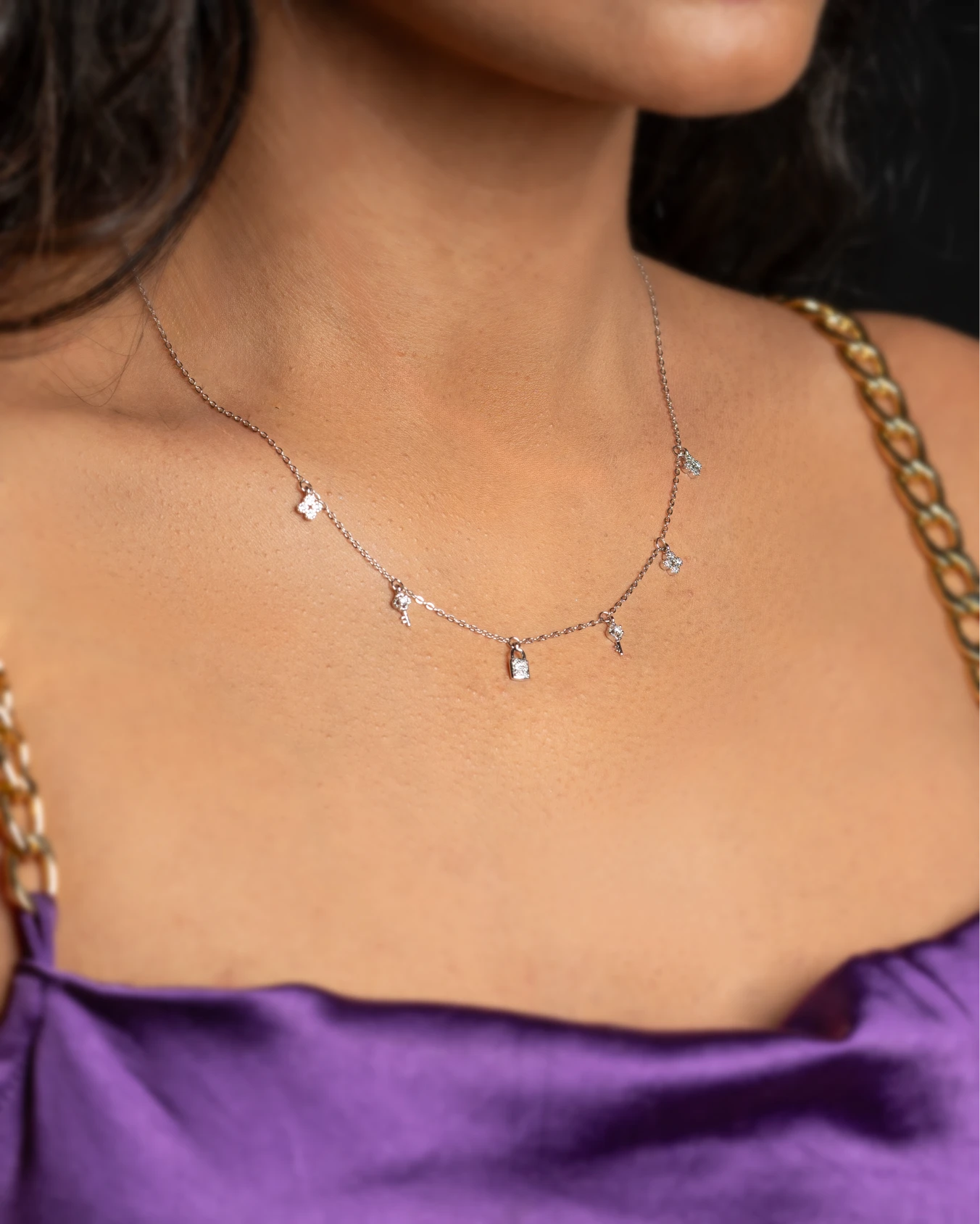 Necklace with small pendants on a woman wearing a purple top.