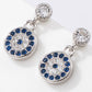 Pair of silver earrings with blue gemstones and clear stones on a white background