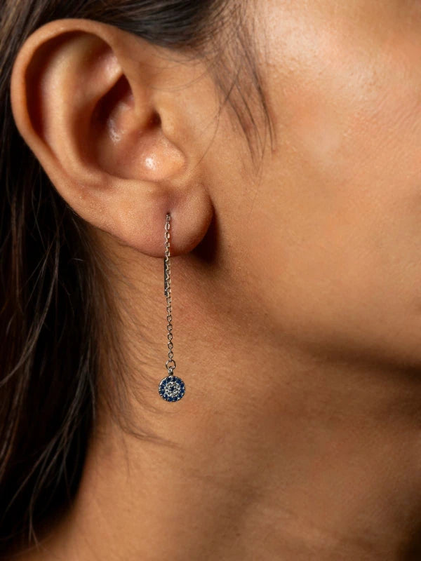 Close-up of an earring with a blue gemstone on a woman's ear.