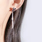 Close-up of an ear wearing a floral earring with a dangling chain on a light background