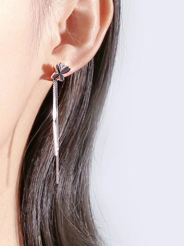 Close-up of an ear wearing a floral earring with a dangling chain on a light background