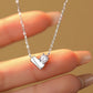 Silver necklace with a heart and diamond pendant held by a hand against a beige background