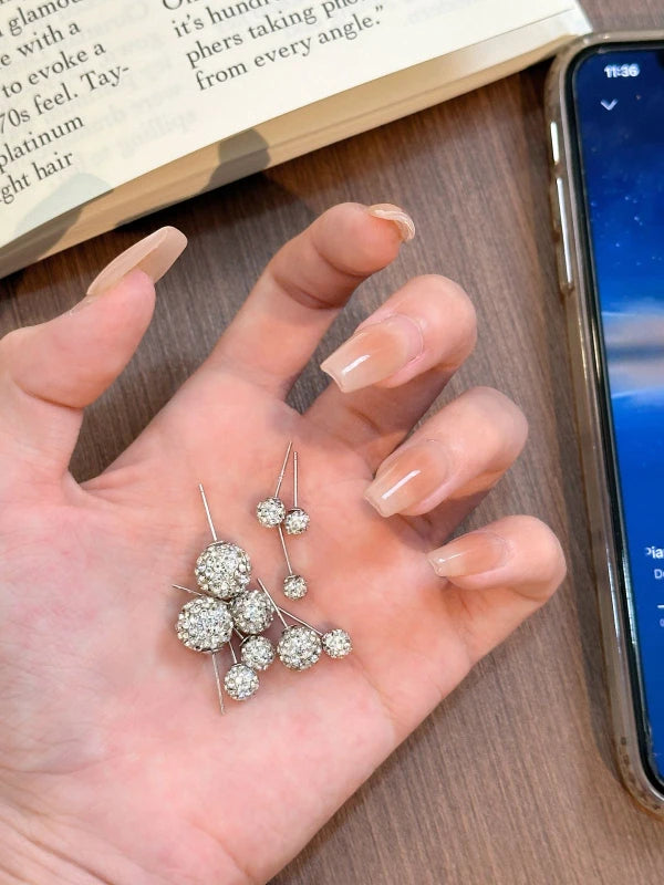 Hand holding a pair of silver earrings with a smartphone and book in the background