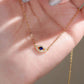 Gold necklace with a blue gemstone pendant held in a hand with light nail polish.