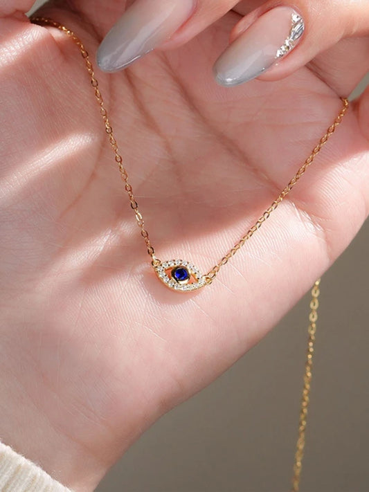 Gold necklace with a blue gemstone pendant held in a hand with light nail polish.