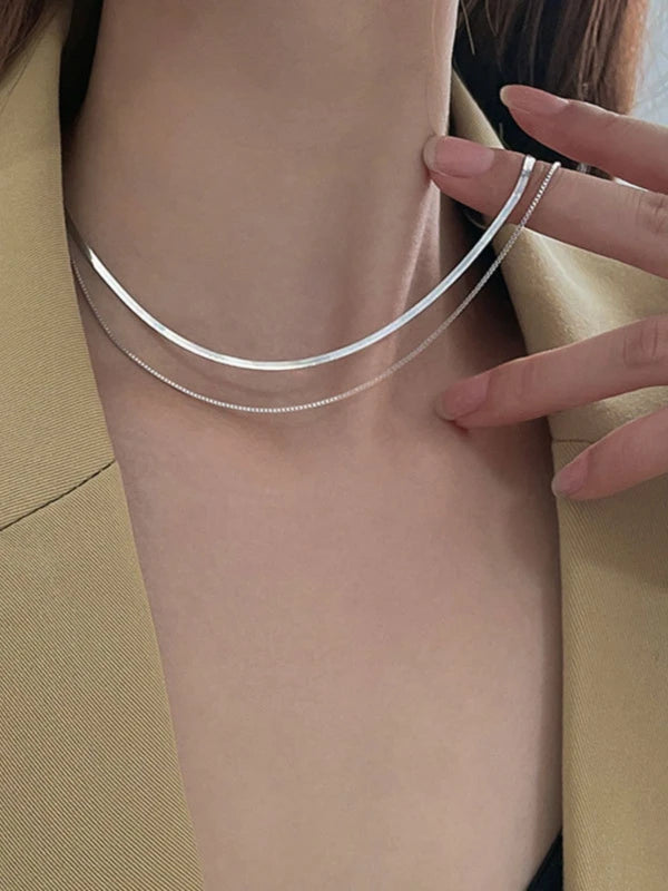 Silver necklace being worn on a person with a neutral background