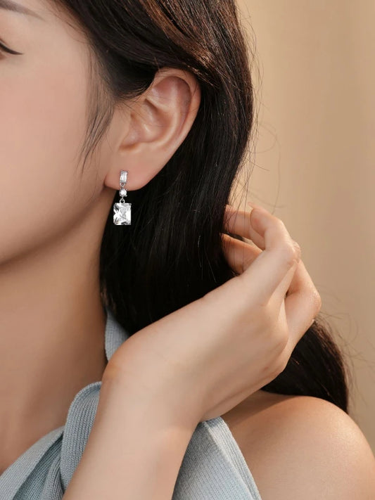 Close-up of a person wearing a diamond earring with a neutral background