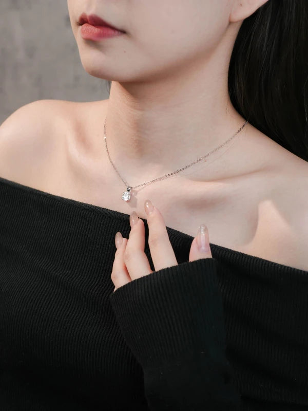 Close-up of a person wearing a necklace with a heart pendant, against a neutral background.