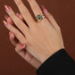 Hand wearing a ring with a green gemstone on a brown background