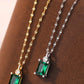 Two emerald green gemstone pendants on gold and silver chains against a brown background