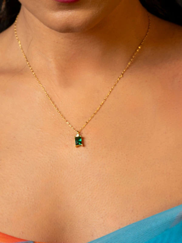 Gold necklace with a green gemstone pendant on a person wearing a blue garment.
