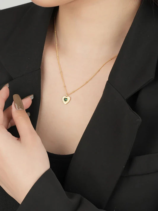 Gold necklace with a heart-shaped pendant worn by a woman in a black outfit.