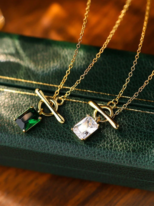 Two gold necklaces with gemstone pendants on a green textured surface.