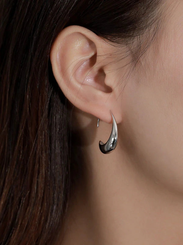 Close-up of an ear wearing a silver hoop earring with a blurred background