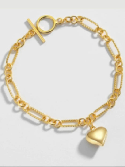 Gold bracelet with a heart charm on a light gray background