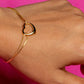 Gold bracelet with a heart-shaped clasp on a wrist against a pink background