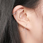 Close-up of an ear with silver earrings against a neutral background