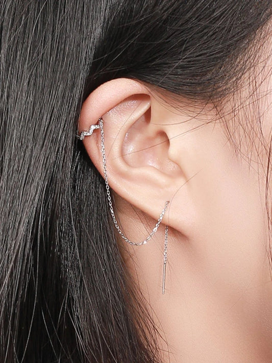 Close-up of an ear with silver earrings against a neutral background