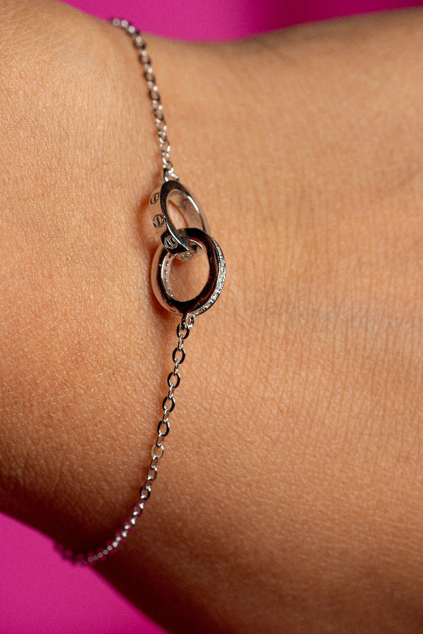 Silver bracelet with interlocking rings on a wrist against a pink background