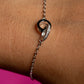 Silver bracelet with a heart-shaped clasp on a wrist against a pink background