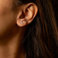 Close-up of an ear wearing a small crescent moon earring with dark hair.