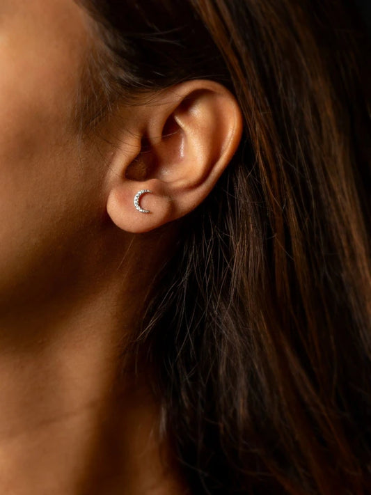 Close-up of an ear wearing a small crescent moon earring with dark hair.