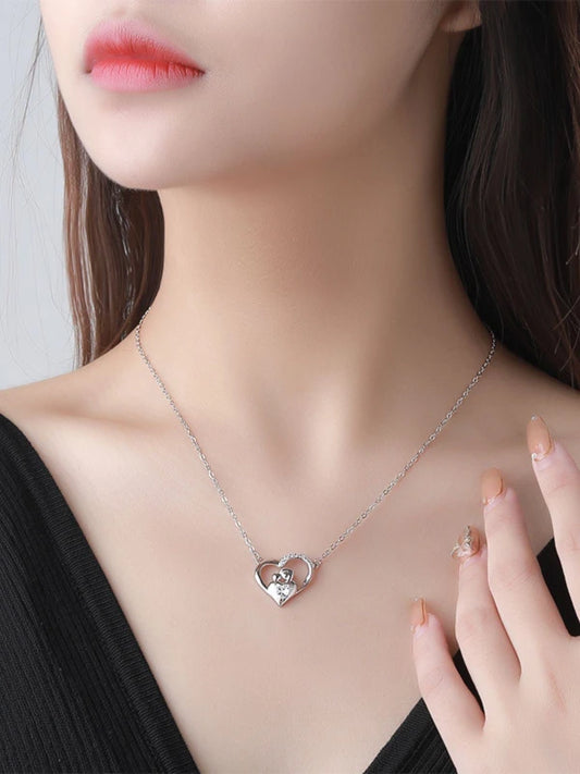 Woman wearing a silver heart-shaped necklace with a clear gemstone.