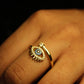 Gold ring with eye design on a finger against a dark background