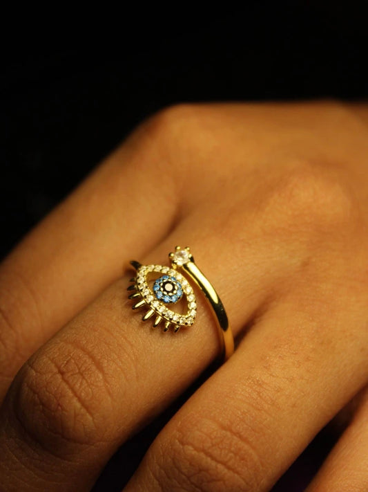Gold ring with eye design on a finger against a dark background