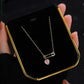 Necklace with a pink gemstone in a gold frame held by hands.